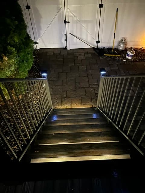 Deck stairs with recessed LED step lighting and black metal railing, photographed at night