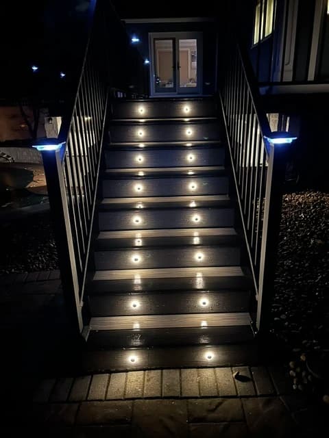 Straight staircase with LED-lit risers and black aluminum railings leading to a home entrance, nighttime