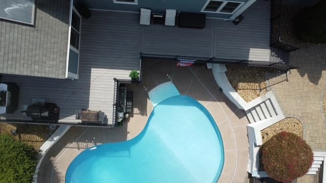 Aerial view of in-ground pool with composite deck and patio area in a residential backyard