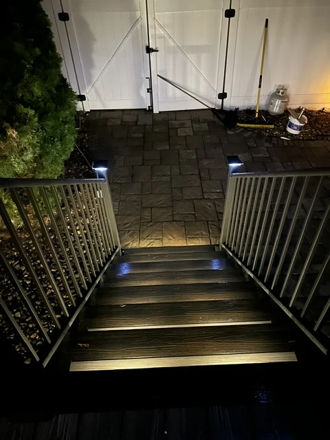Deck stairs with recessed LED step lighting and black metal railing, photographed at night