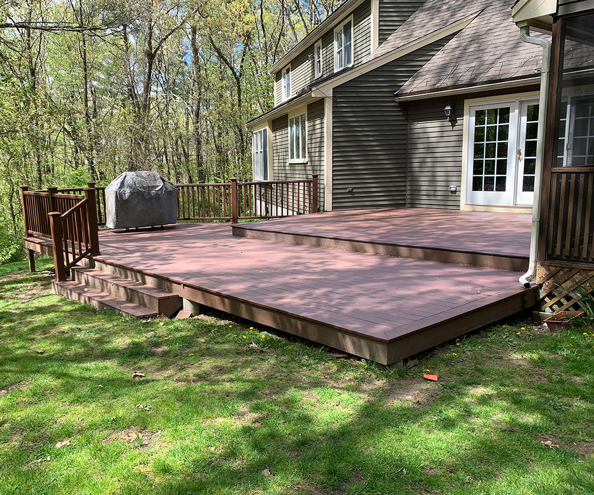 A deck with a grill overlooking a house in the background.