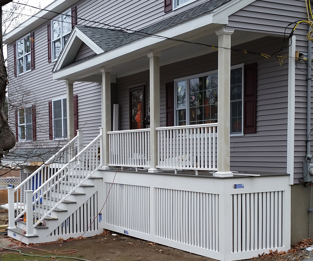 A two-story house with gray siding, a white railing porch, and stairs leading up to the front door.